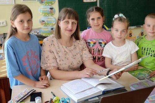 A teacher with four students in a classroom encouraging education and learning.